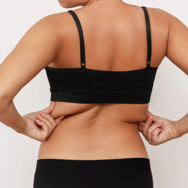 Cropped shot of a young tanned woman in black underwear holding fat folds on her back isolated on a white background. Overweight, flabby and sagging muscles